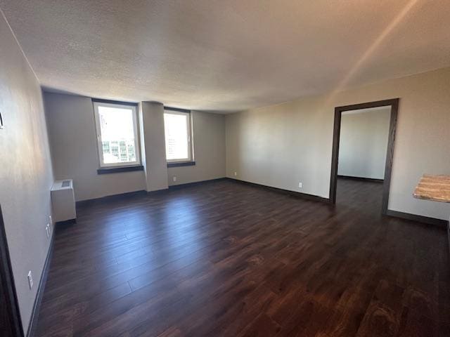 unfurnished room with dark wood-style floors, radiator heating unit, baseboards, and a textured ceiling