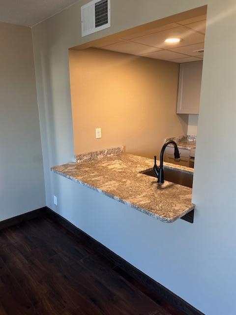 kitchen featuring a drop ceiling, dark wood-type flooring, a sink, visible vents, and baseboards