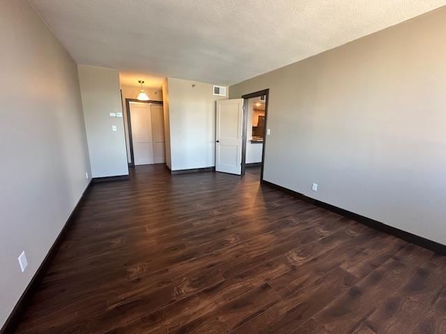 unfurnished room featuring visible vents, dark wood finished floors, a textured ceiling, and baseboards