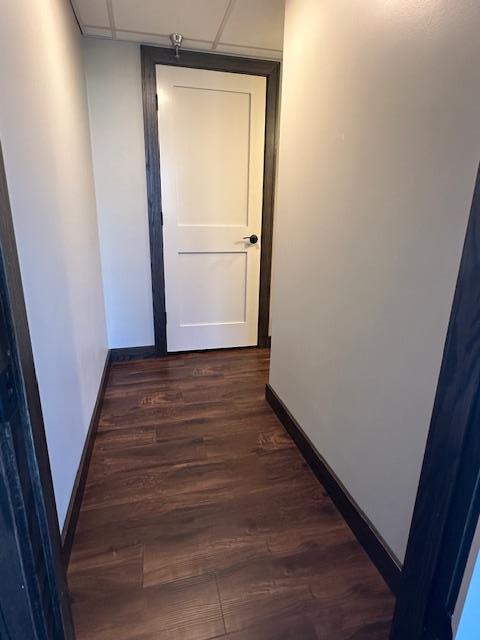 hall with dark wood-type flooring, a drop ceiling, and baseboards