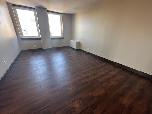 unfurnished room with dark wood-style floors, radiator, and baseboards