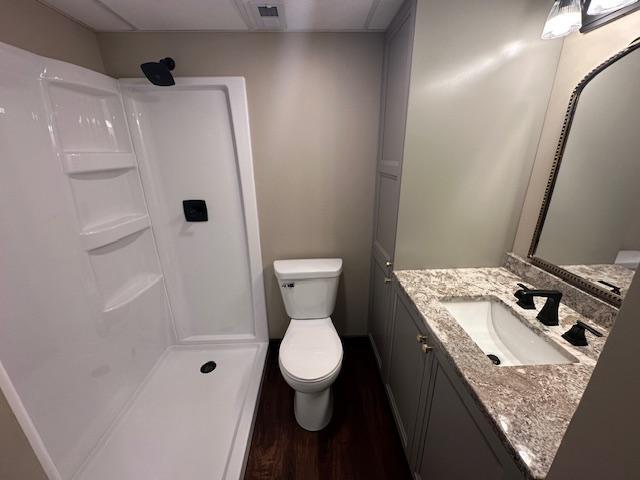 bathroom featuring a shower, wood finished floors, vanity, and toilet