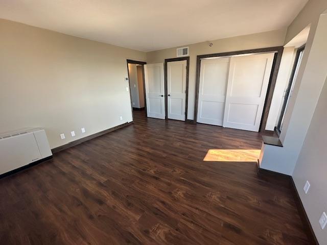 unfurnished bedroom with dark wood-style floors, baseboards, visible vents, and multiple closets