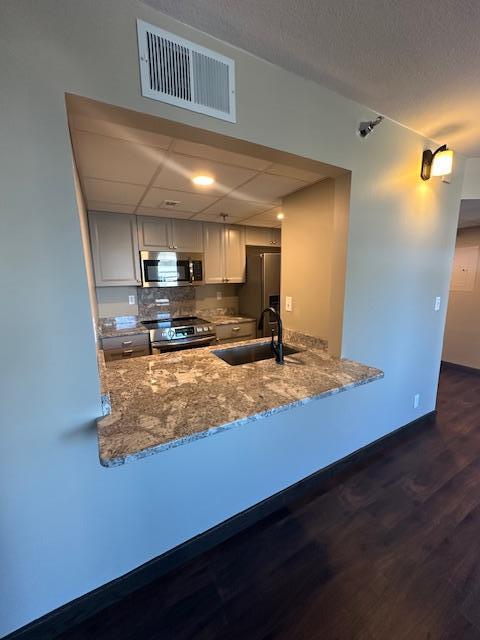 kitchen featuring stone counters, visible vents, appliances with stainless steel finishes, a sink, and a peninsula