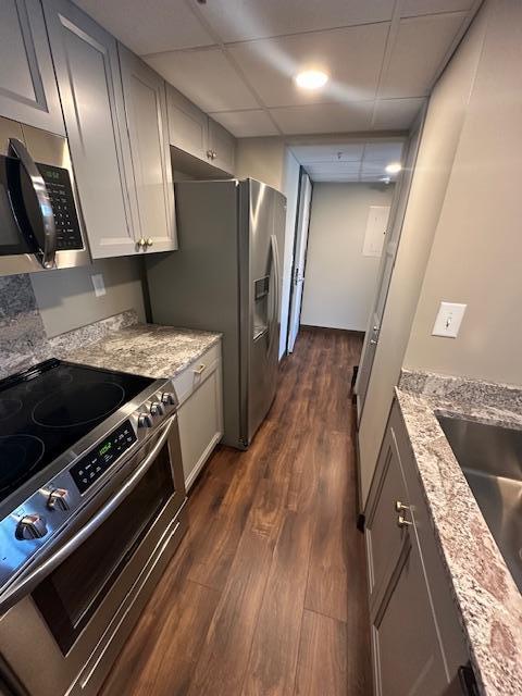 kitchen with dark wood finished floors, stainless steel appliances, a paneled ceiling, a sink, and light stone countertops