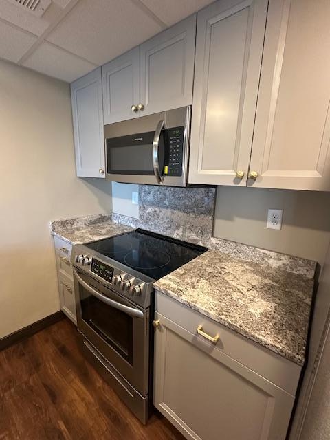 kitchen featuring baseboards, a drop ceiling, dark wood-style floors, appliances with stainless steel finishes, and light stone countertops