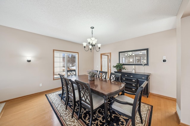 dining space with an inviting chandelier, light wood-type flooring, and a textured ceiling