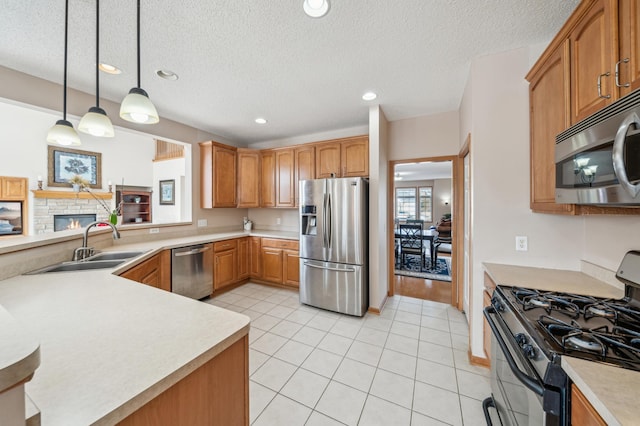 kitchen with a sink, appliances with stainless steel finishes, a fireplace, light countertops, and hanging light fixtures