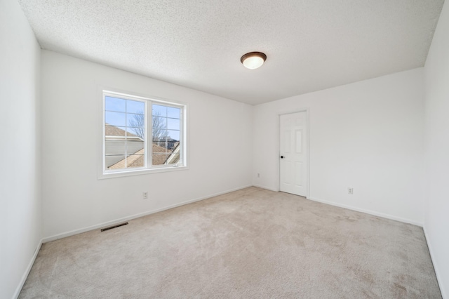 carpeted spare room featuring visible vents, a textured ceiling, and baseboards