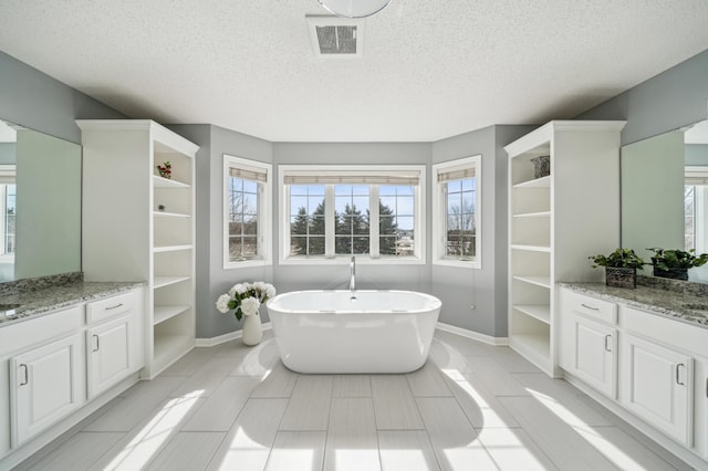 bathroom featuring vanity, a soaking tub, baseboards, and a textured ceiling