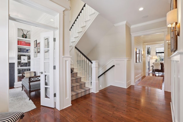 stairs featuring a wainscoted wall, built in shelves, wood finished floors, crown molding, and a decorative wall