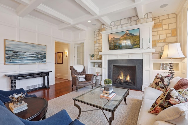 living room featuring beamed ceiling, coffered ceiling, wood finished floors, a lit fireplace, and a decorative wall