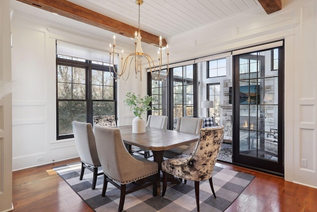 dining room featuring hardwood / wood-style floors, a notable chandelier, beamed ceiling, and a decorative wall