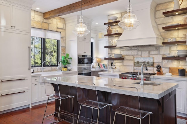 kitchen featuring a center island with sink, open shelves, white cabinetry, decorative backsplash, and custom exhaust hood