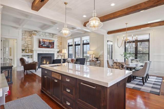 kitchen with a lit fireplace, beam ceiling, an inviting chandelier, dark wood-style floors, and a sink