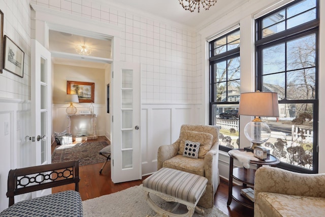 living area with wood finished floors, french doors, wainscoting, crown molding, and a decorative wall