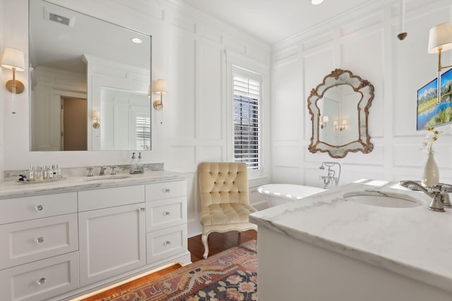 full bath featuring vanity, wood finished floors, visible vents, ornamental molding, and a decorative wall