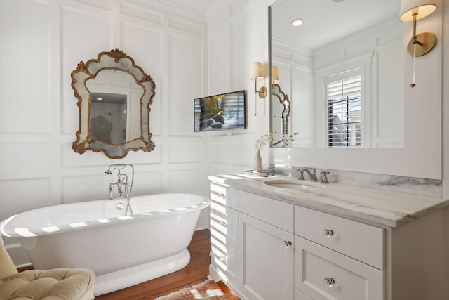 full bath featuring vanity, a soaking tub, a decorative wall, and wood finished floors