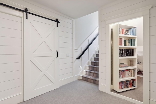 stairs with a barn door and carpet floors