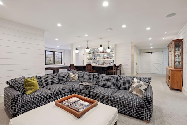 living area featuring recessed lighting, a bar, wood walls, light carpet, and a barn door