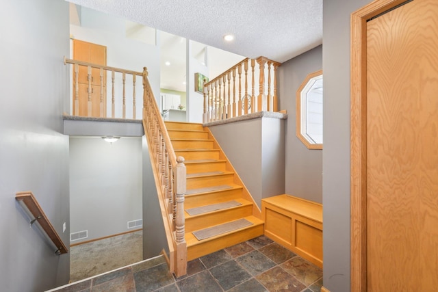 staircase with visible vents, baseboards, a textured ceiling, and stone finish flooring