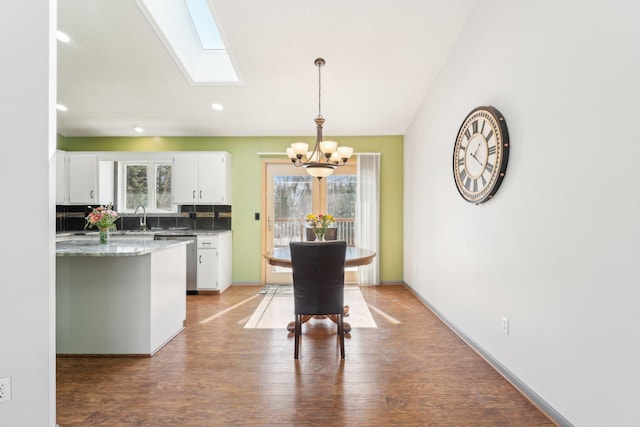 dining space featuring baseboards, a chandelier, recessed lighting, a skylight, and light wood-style floors