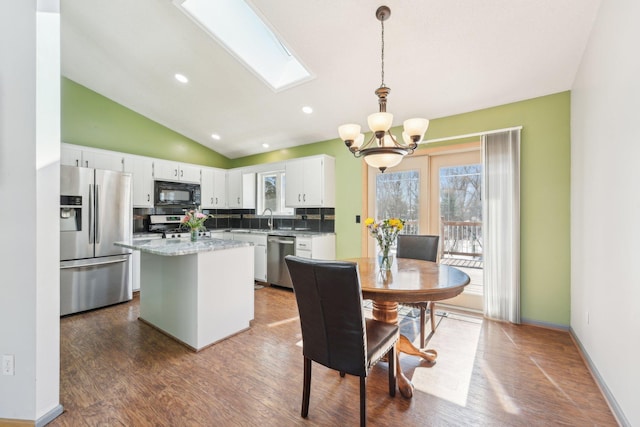 dining area featuring recessed lighting, vaulted ceiling with skylight, an inviting chandelier, baseboards, and dark wood-style flooring