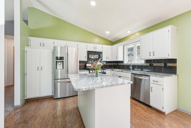 kitchen featuring tasteful backsplash, lofted ceiling, appliances with stainless steel finishes, wood finished floors, and a sink