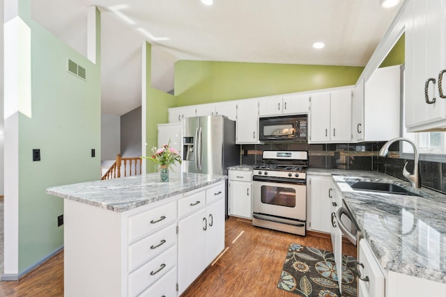 kitchen with visible vents, a kitchen island, a sink, vaulted ceiling, and appliances with stainless steel finishes