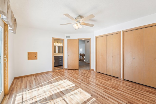 unfurnished bedroom featuring visible vents, baseboards, multiple closets, light wood-type flooring, and ensuite bathroom