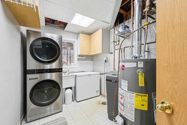 laundry room featuring water heater, cabinet space, stacked washer / drying machine, baseboards, and light floors