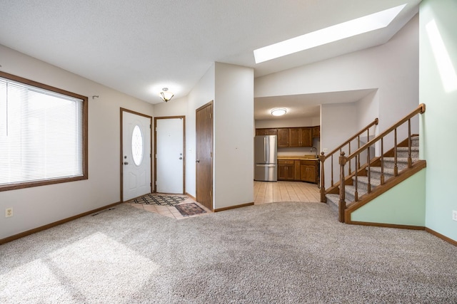 entrance foyer featuring stairway, baseboards, a textured ceiling, lofted ceiling with skylight, and light carpet