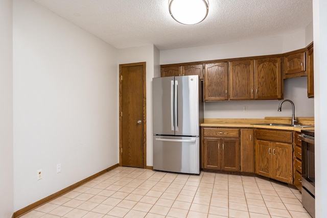 kitchen featuring light countertops, light tile patterned floors, appliances with stainless steel finishes, a textured ceiling, and a sink