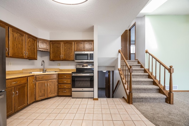 kitchen with brown cabinetry, visible vents, a sink, stainless steel appliances, and light countertops