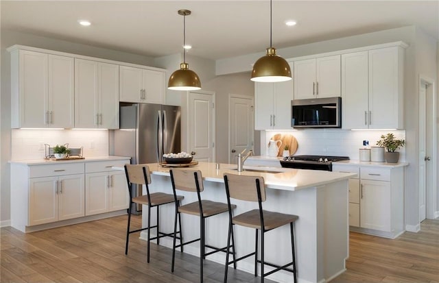 kitchen featuring light wood-style flooring, stainless steel appliances, white cabinetry, light countertops, and an island with sink