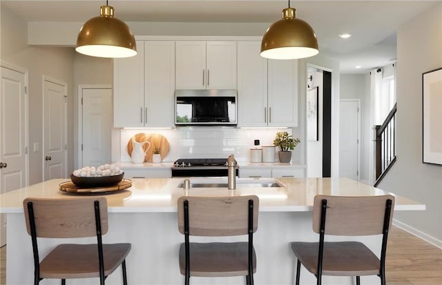 kitchen with stainless steel appliances, hanging light fixtures, backsplash, light wood-style flooring, and a sink