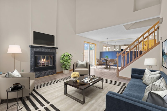 living area featuring stairway, wood finished floors, an inviting chandelier, a high ceiling, and a fireplace