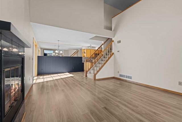 unfurnished living room with visible vents, a notable chandelier, wood finished floors, baseboards, and stairs