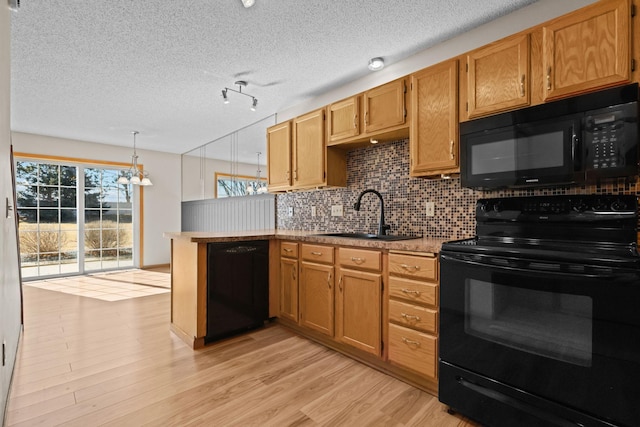 kitchen with black appliances, light wood-style flooring, a sink, backsplash, and a peninsula