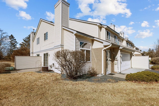 back of property with central AC unit, driveway, a chimney, a garage, and brick siding