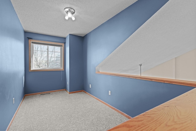 carpeted empty room featuring visible vents, a textured ceiling, and baseboards