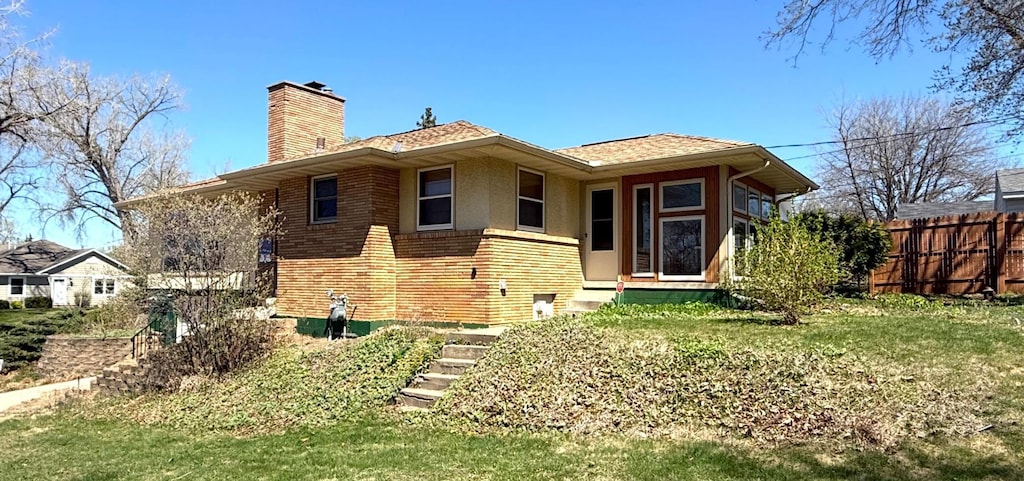rear view of house with a chimney, brick siding, fence, a yard, and stucco siding