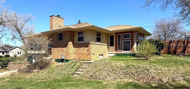 rear view of house with a chimney, brick siding, fence, a yard, and stucco siding