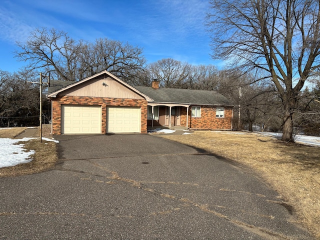 single story home with a chimney, brick siding, an attached garage, and driveway