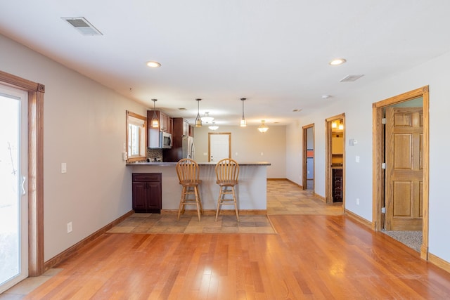 kitchen featuring visible vents, decorative light fixtures, light wood-style flooring, appliances with stainless steel finishes, and a peninsula