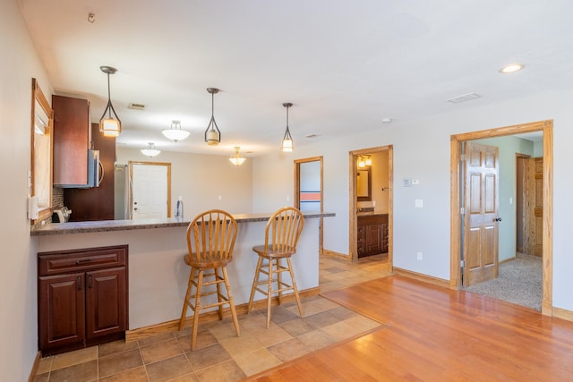 kitchen featuring light wood-type flooring, visible vents, a peninsula, a breakfast bar area, and hanging light fixtures