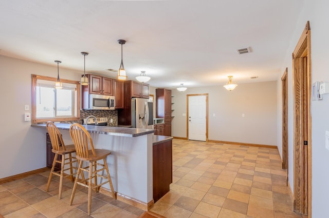 kitchen with visible vents, dark countertops, backsplash, stainless steel appliances, and a peninsula