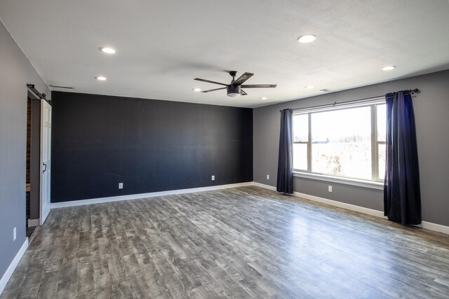 empty room with ceiling fan, baseboards, a barn door, recessed lighting, and wood finished floors