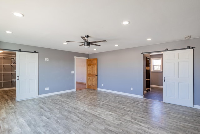 interior space with a barn door, recessed lighting, wood finished floors, and baseboards