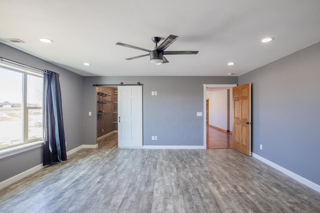 unfurnished bedroom with wood finished floors, baseboards, visible vents, recessed lighting, and a barn door